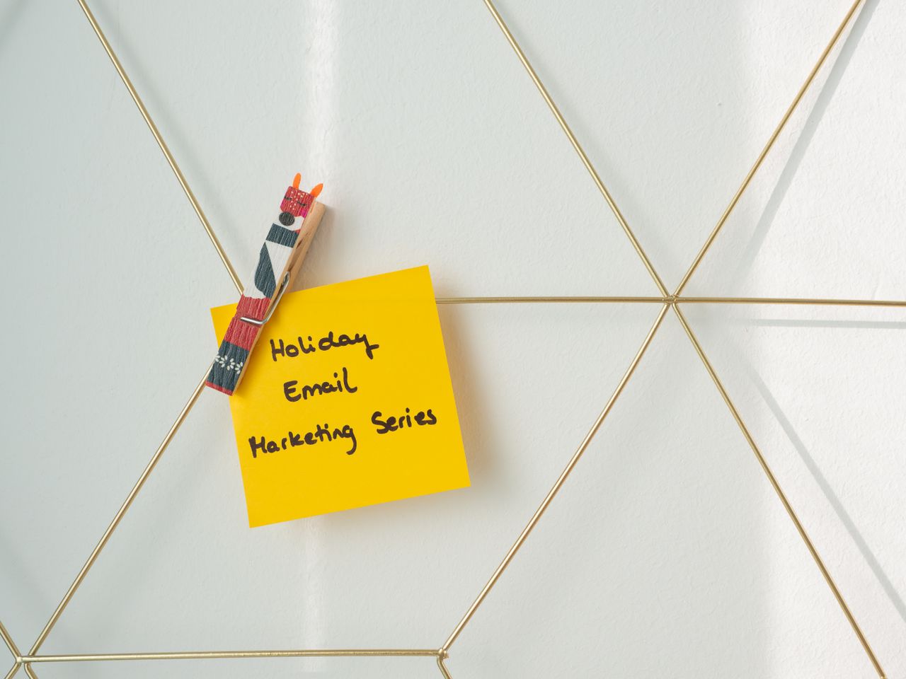 Bright yellow sticky note clipped to a wireframe wall, featuring a holiday email marketing message.
